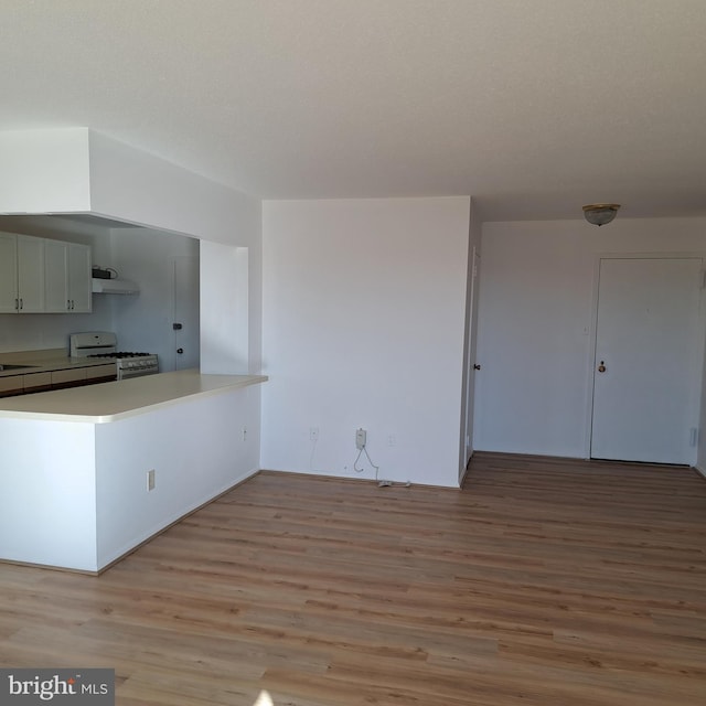 kitchen with white gas range oven, light hardwood / wood-style floors, white cabinetry, and range hood