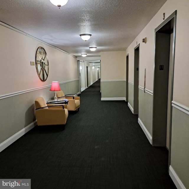 hall featuring dark carpet, a textured ceiling, and elevator