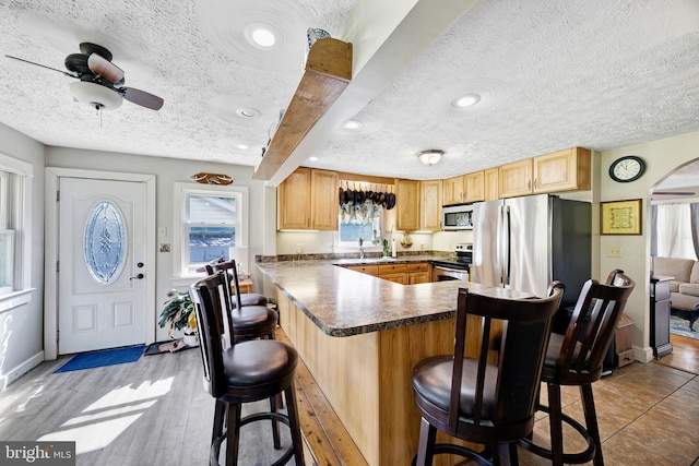 kitchen featuring kitchen peninsula, appliances with stainless steel finishes, a kitchen breakfast bar, a healthy amount of sunlight, and wood-type flooring