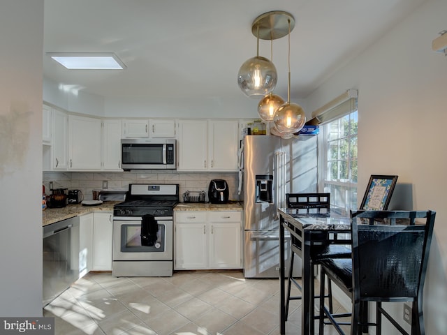 kitchen with white cabinets, decorative light fixtures, light stone counters, and stainless steel appliances