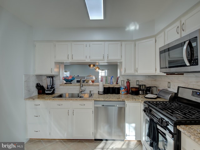 kitchen with white cabinets, sink, appliances with stainless steel finishes, light tile patterned flooring, and light stone counters