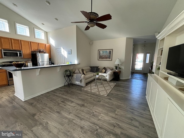 kitchen with dark wood-type flooring, high vaulted ceiling, kitchen peninsula, a breakfast bar, and appliances with stainless steel finishes