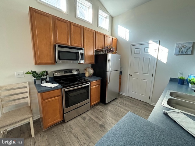 kitchen with high vaulted ceiling, sink, appliances with stainless steel finishes, and light hardwood / wood-style flooring