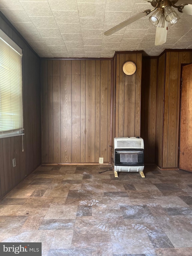 unfurnished room with ceiling fan, heating unit, and wooden walls