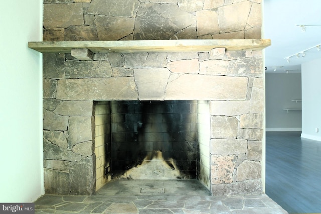 room details featuring rail lighting, hardwood / wood-style flooring, and a stone fireplace