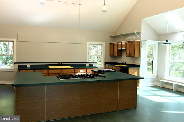 kitchen featuring dark wood-type flooring, sink, stainless steel gas cooktop, lofted ceiling with skylight, and decorative light fixtures