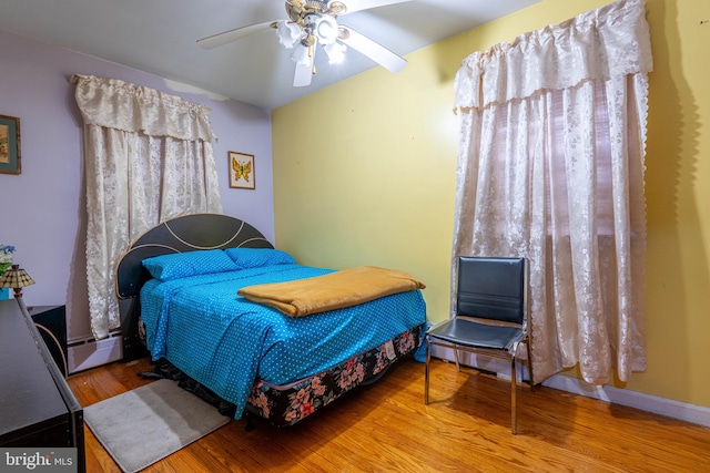 bedroom featuring wood-type flooring, baseboard heating, and ceiling fan