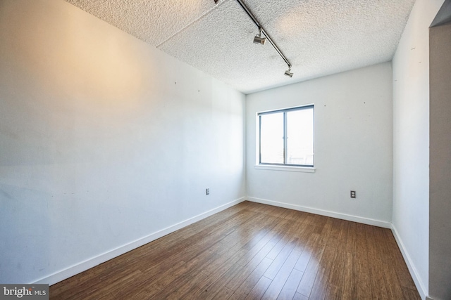 spare room featuring baseboards, dark wood-style flooring, a textured ceiling, and track lighting