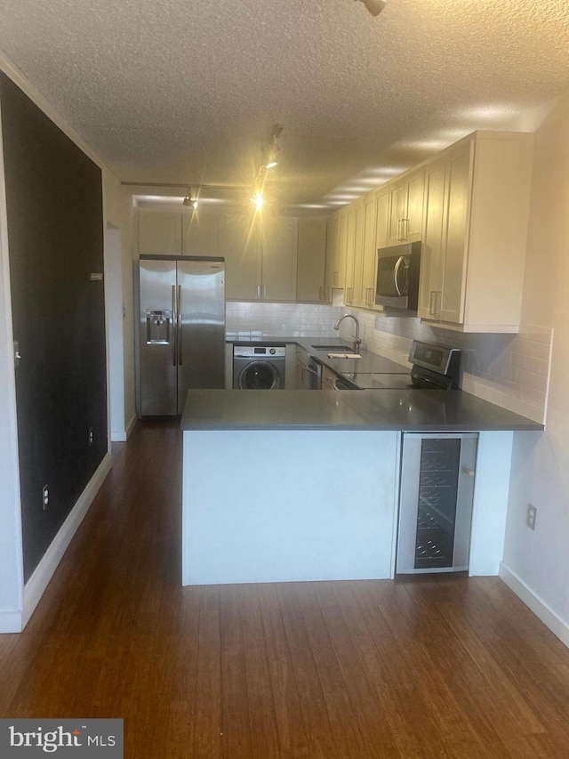 kitchen with washer / dryer, kitchen peninsula, backsplash, sink, and stainless steel appliances