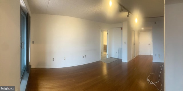 empty room with a textured ceiling, dark wood-type flooring, and rail lighting