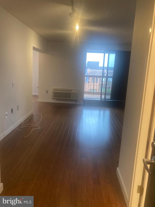 unfurnished living room with an AC wall unit, a textured ceiling, and dark hardwood / wood-style floors