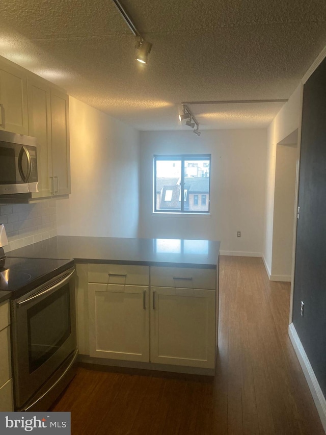 kitchen with dark wood-type flooring, kitchen peninsula, stainless steel appliances, rail lighting, and a textured ceiling