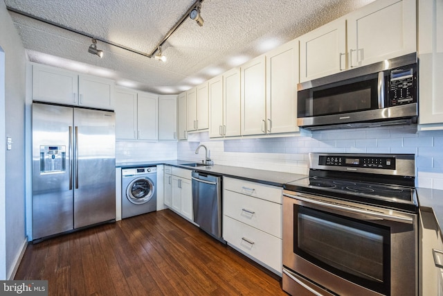 kitchen with washer / clothes dryer, dark wood finished floors, track lighting, backsplash, and stainless steel appliances
