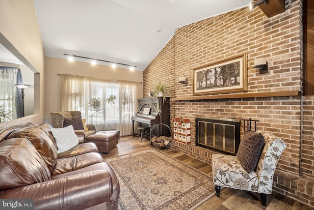 living room featuring wood-type flooring, brick wall, vaulted ceiling, rail lighting, and a fireplace