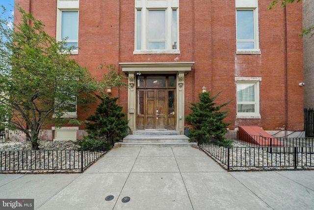 view of exterior entry featuring brick siding and fence