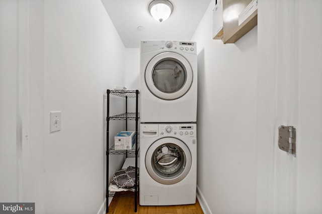 laundry area featuring stacked washer and dryer, baseboards, light wood-type flooring, and laundry area