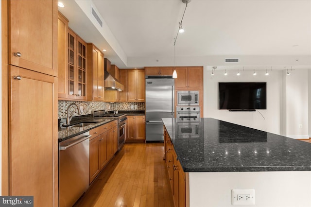 kitchen featuring sink, dark stone countertops, a center island, built in appliances, and wall chimney range hood