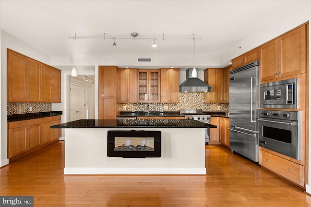 kitchen featuring pendant lighting, wall chimney exhaust hood, built in appliances, and a kitchen island