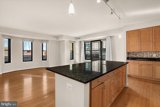 kitchen with pendant lighting, decorative backsplash, dark stone counters, light hardwood / wood-style floors, and track lighting