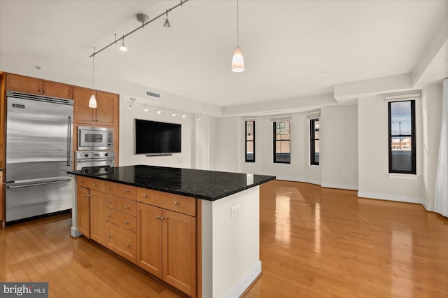 kitchen featuring light hardwood / wood-style flooring, hanging light fixtures, a center island, built in appliances, and dark stone counters