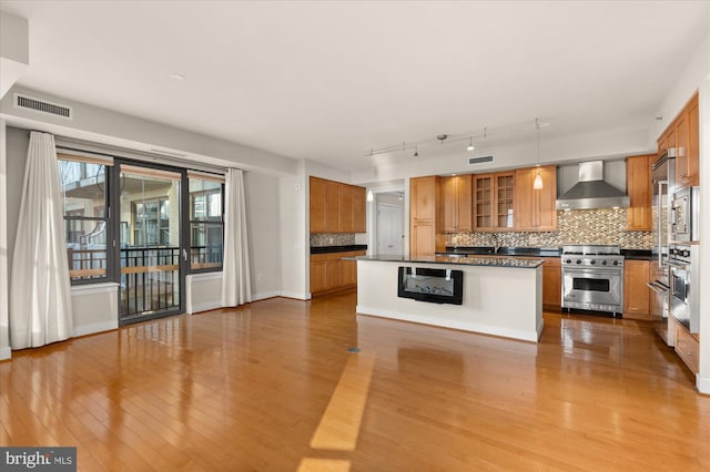 kitchen with appliances with stainless steel finishes, decorative light fixtures, rail lighting, a center island, and wall chimney range hood