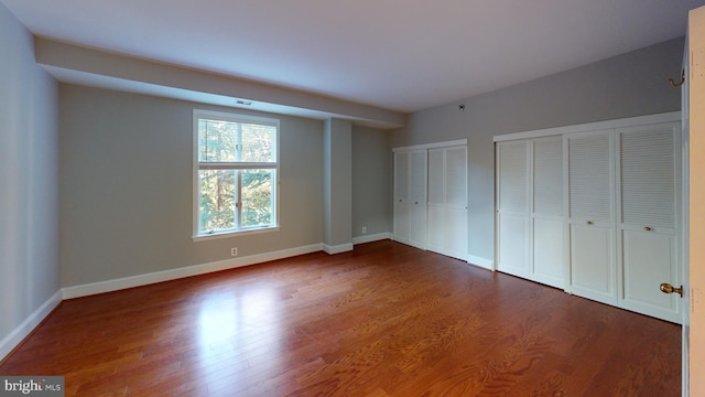 unfurnished bedroom with hardwood / wood-style flooring and two closets