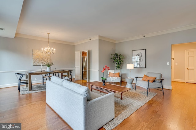 living room with ornamental molding, an inviting chandelier, and light hardwood / wood-style flooring