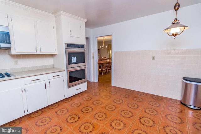 kitchen with stainless steel double oven, gas cooktop, hanging light fixtures, an inviting chandelier, and white cabinets