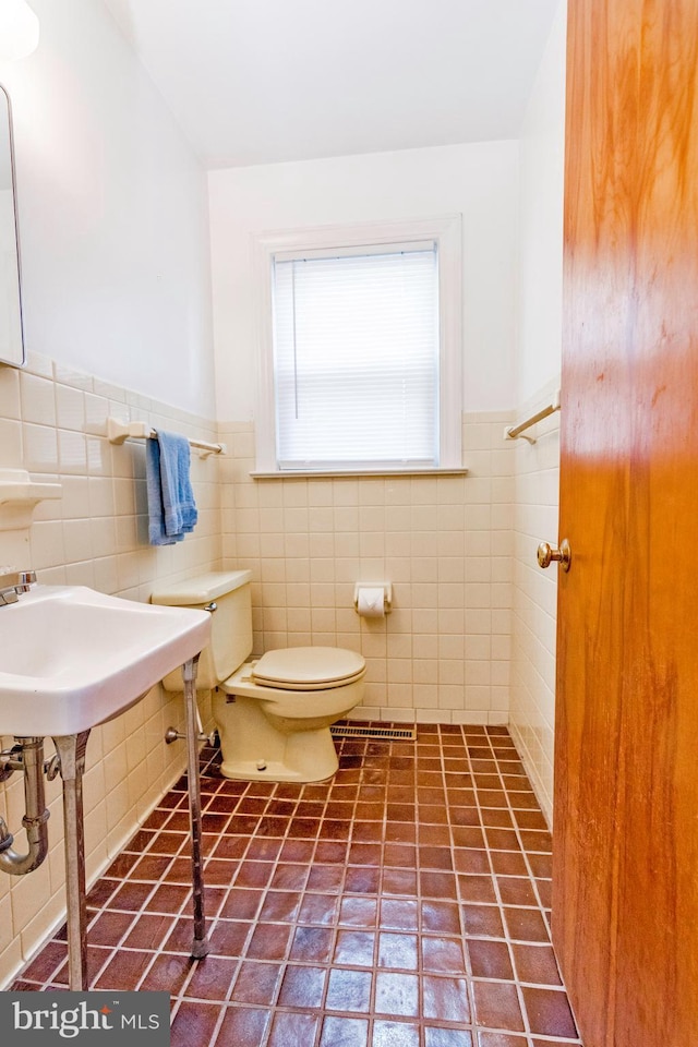half bath with tile walls, toilet, and wainscoting