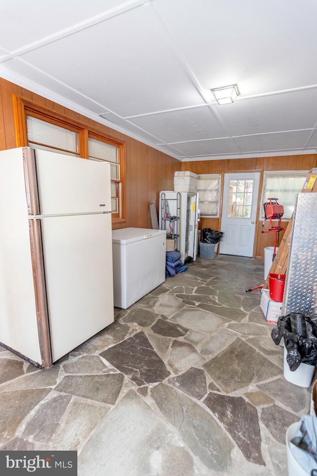 kitchen featuring wooden walls, freestanding refrigerator, stone flooring, and fridge