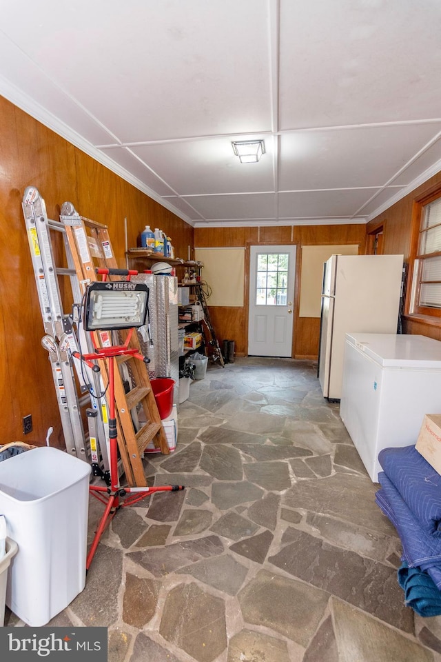 below grade area with wooden walls, freestanding refrigerator, white refrigerator, and stone floors