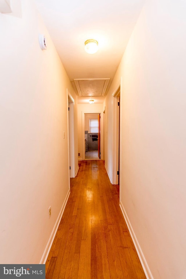 hall with attic access, light wood-style floors, and baseboards
