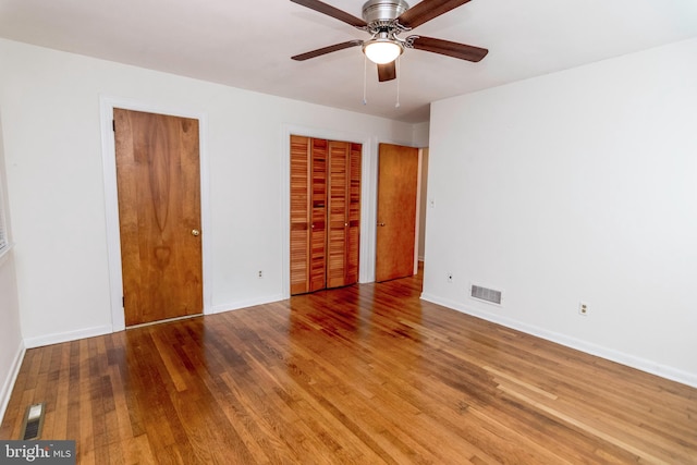 unfurnished bedroom featuring two closets, hardwood / wood-style flooring, and ceiling fan