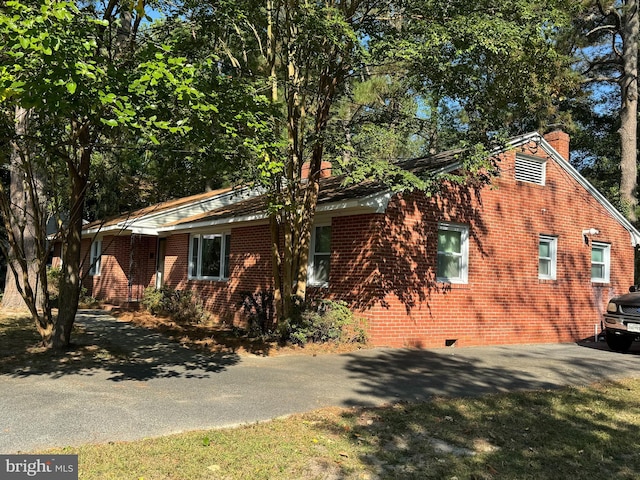 view of side of home featuring aphalt driveway, a chimney, brick siding, and crawl space