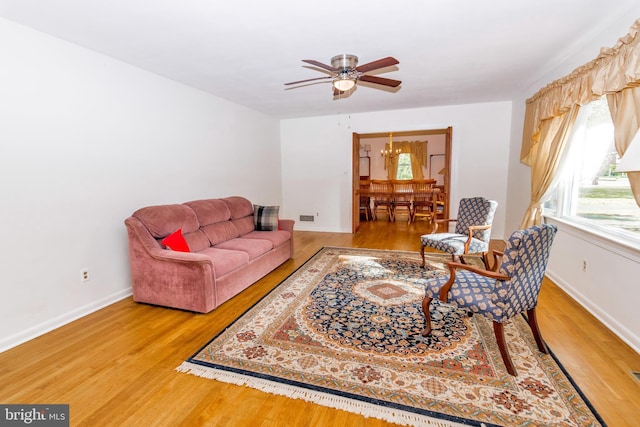living area with wood finished floors, a healthy amount of sunlight, and ceiling fan with notable chandelier
