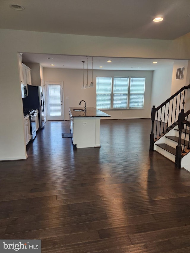 kitchen featuring dark hardwood / wood-style flooring, decorative light fixtures, an island with sink, appliances with stainless steel finishes, and white cabinetry