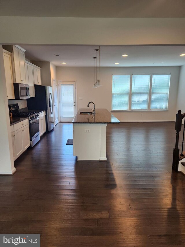 kitchen featuring appliances with stainless steel finishes, pendant lighting, white cabinetry, and an island with sink