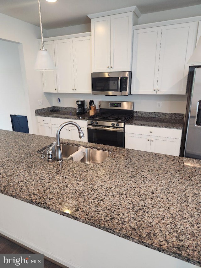 kitchen featuring pendant lighting, dark stone counters, sink, stainless steel appliances, and white cabinets