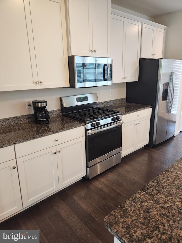 kitchen with dark stone countertops, stainless steel appliances, dark hardwood / wood-style floors, and white cabinetry