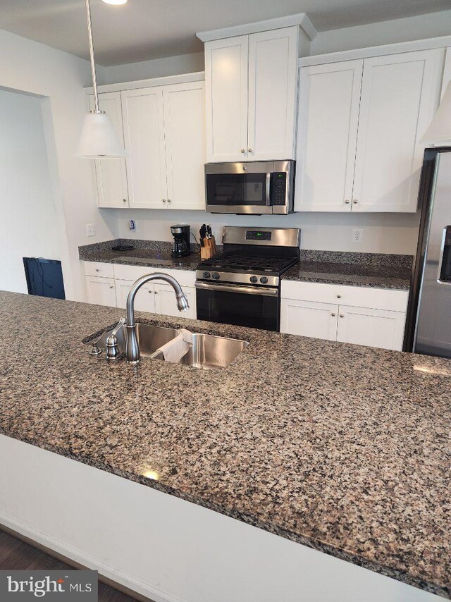 kitchen with hanging light fixtures, sink, white cabinetry, appliances with stainless steel finishes, and dark stone countertops