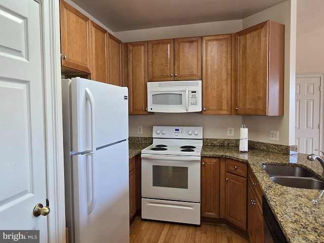 kitchen featuring dark stone countertops, sink, light wood-type flooring, and white appliances