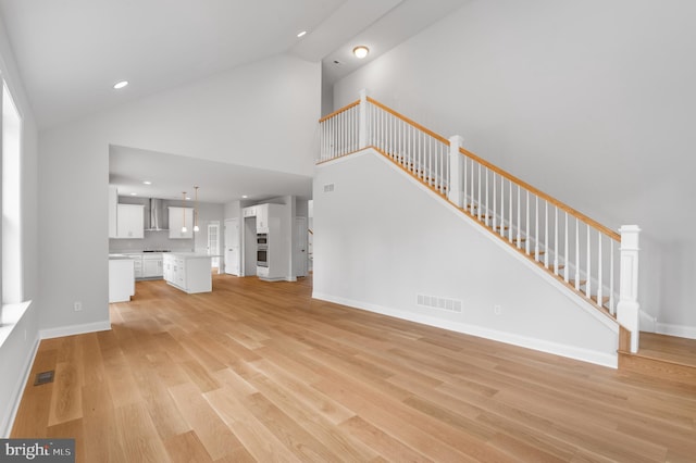 unfurnished living room with stairs, high vaulted ceiling, light wood finished floors, and visible vents