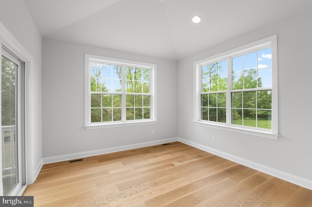 empty room featuring lofted ceiling, light hardwood / wood-style flooring, and a healthy amount of sunlight