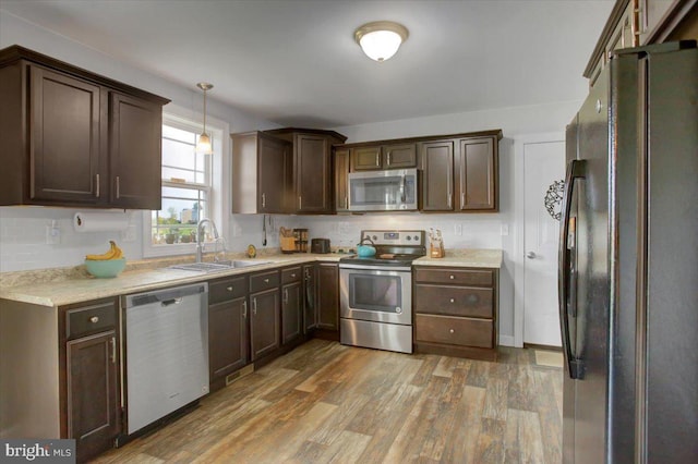 kitchen featuring pendant lighting, dark brown cabinetry, sink, stainless steel appliances, and hardwood / wood-style flooring