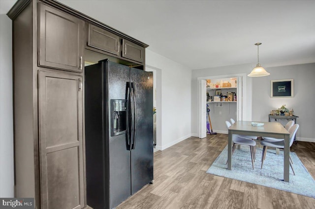 kitchen with pendant lighting, light hardwood / wood-style floors, dark brown cabinetry, and black fridge with ice dispenser