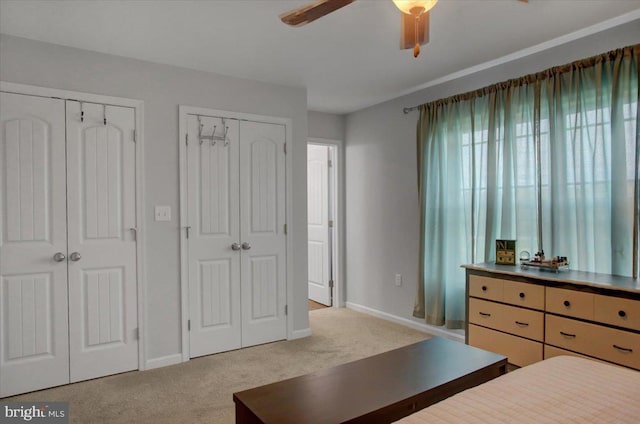 bedroom featuring ceiling fan, multiple closets, and light carpet