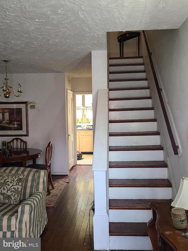 stairway featuring a chandelier, wood-type flooring, and a textured ceiling