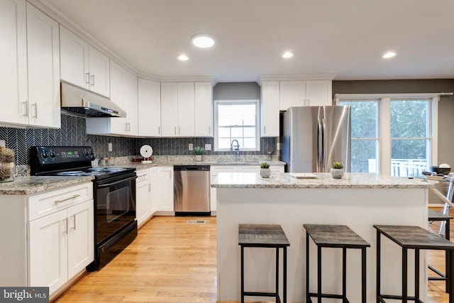 kitchen with light hardwood / wood-style floors, stainless steel appliances, a breakfast bar, and white cabinets