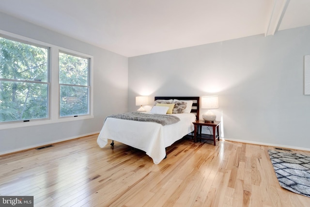 bedroom featuring beam ceiling and light hardwood / wood-style flooring