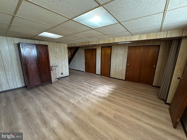 basement featuring light hardwood / wood-style floors, wood walls, and a paneled ceiling